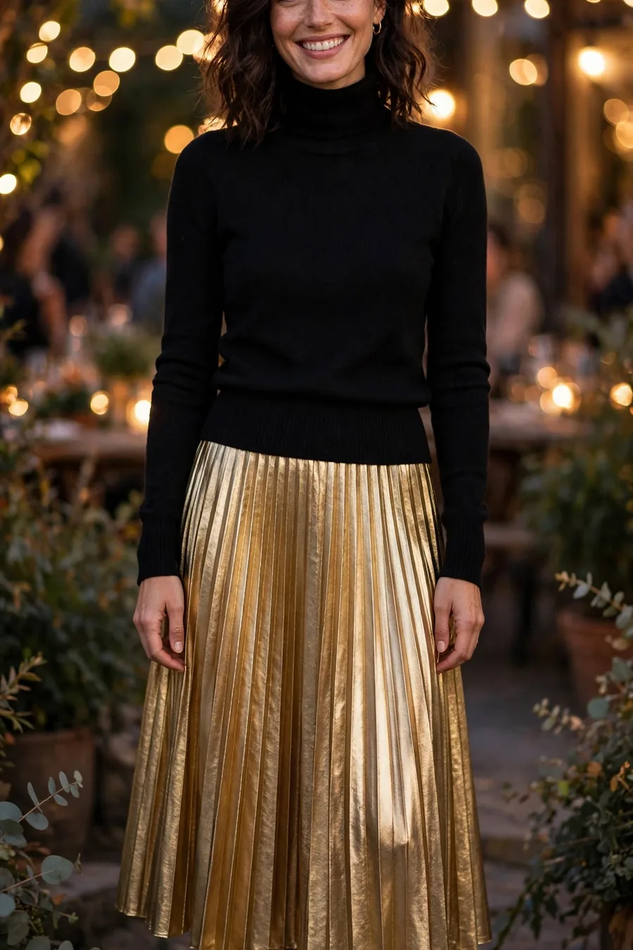 Woman wearing gold pleated metallic midi skirt with black turtleneck at a festive evening party
