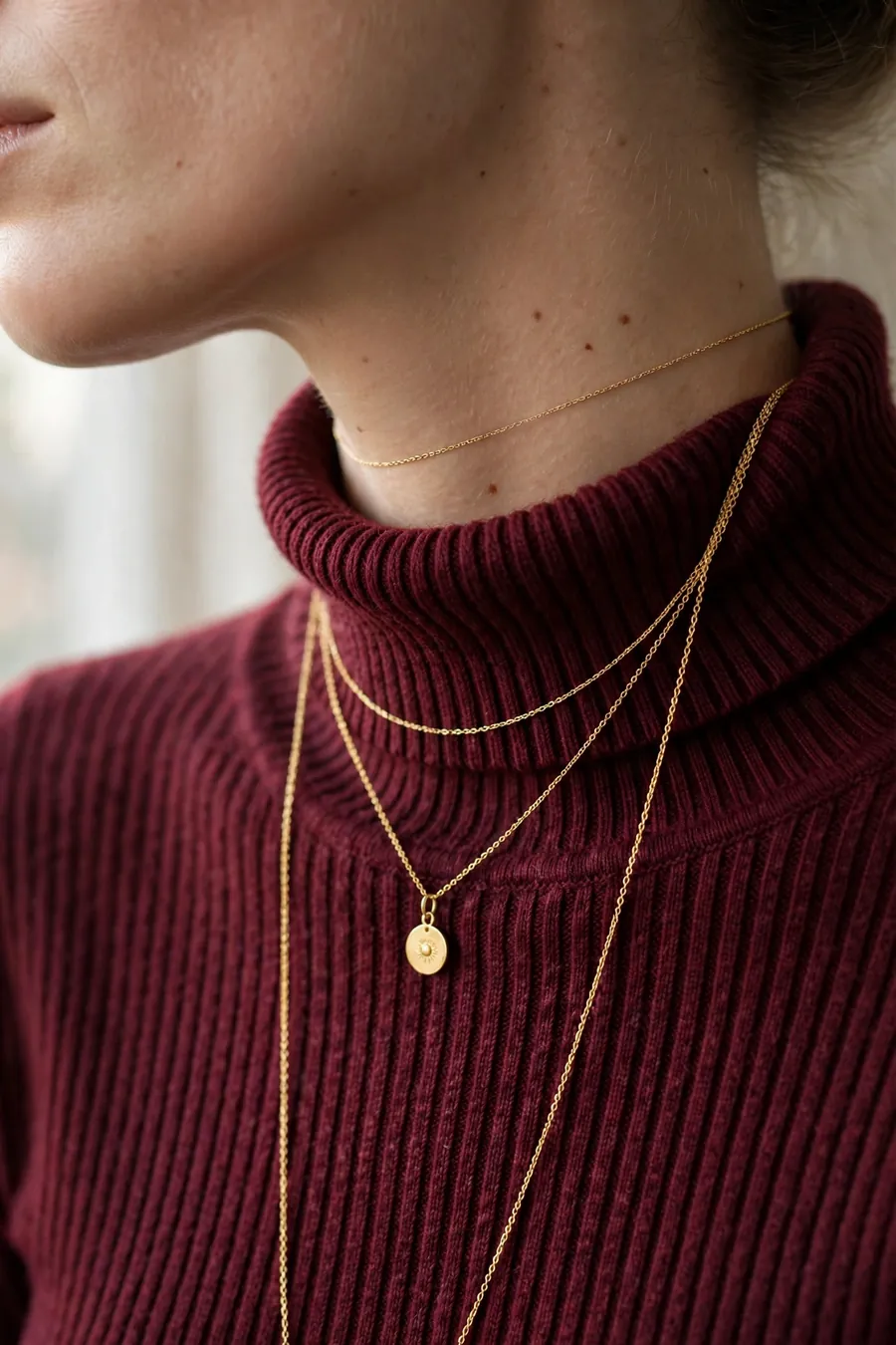 Layered gold necklaces styled over a ribbed burgundy turtleneck, close up